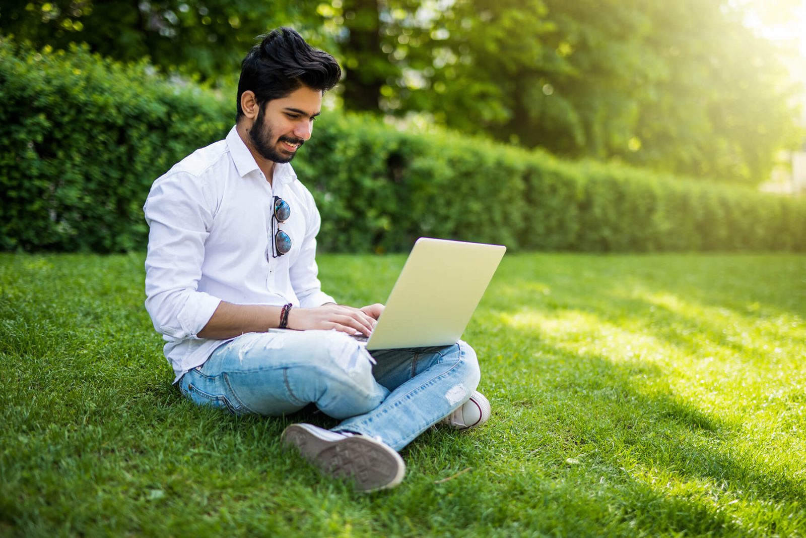Young distance learning student sitting in grass studying on laptop