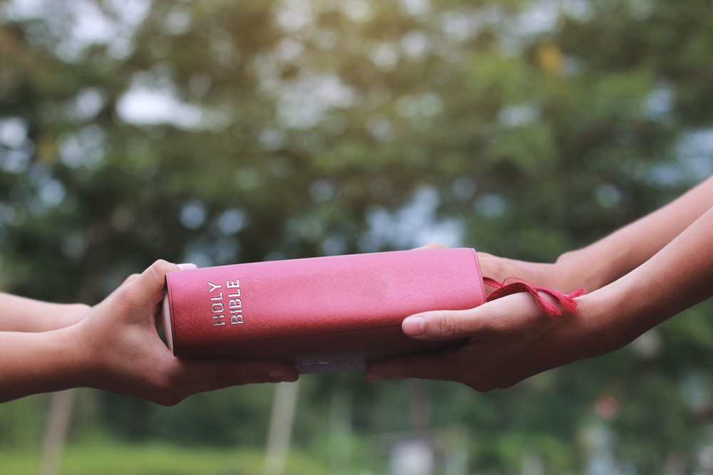 Two sets of hands touching a Bible representing evangelism