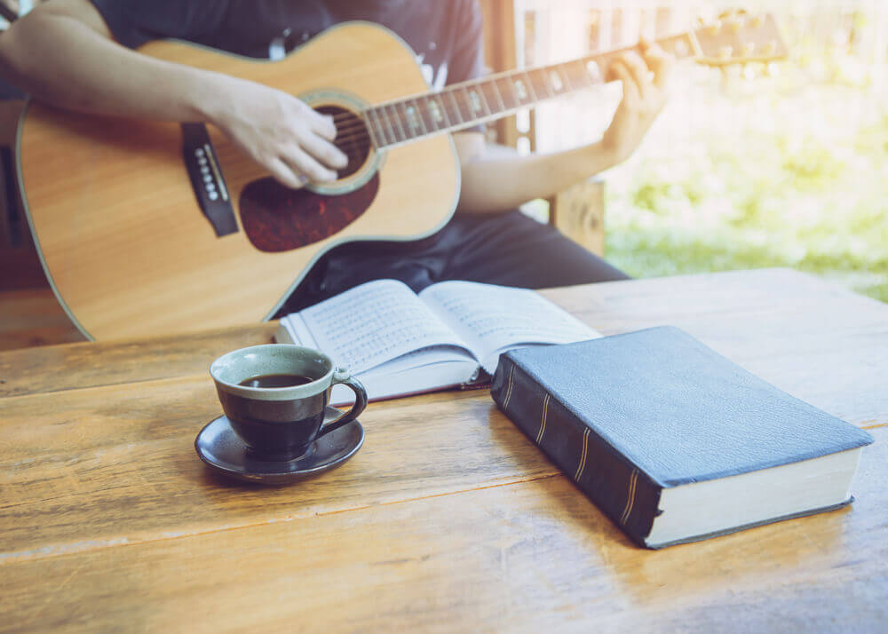 Man player a guitar in front of a bible and hymnal on coffee table