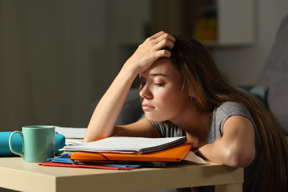 Tired female distance learning student leaning over books on desk