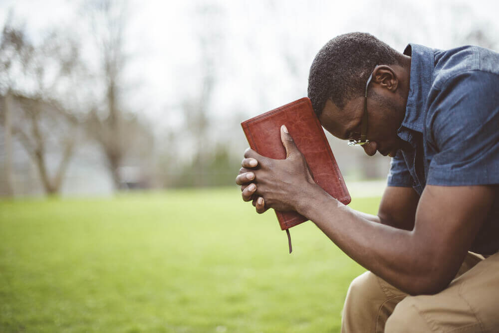 Young, stressed out distance learning student, head bowed holding bible