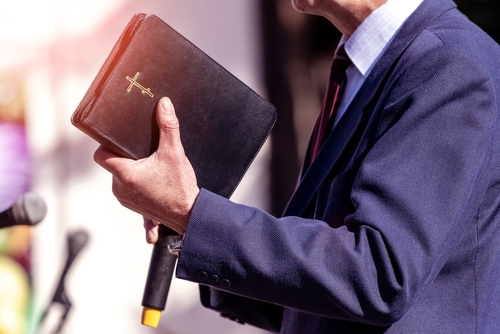 Christian minister holding a Bible and microphone.