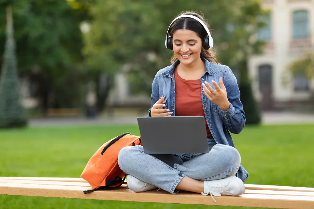 Student smiling in front of a laptop while studying outside on campus