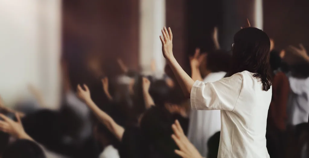 Photo shows Christians worshiping with raised hands in a service